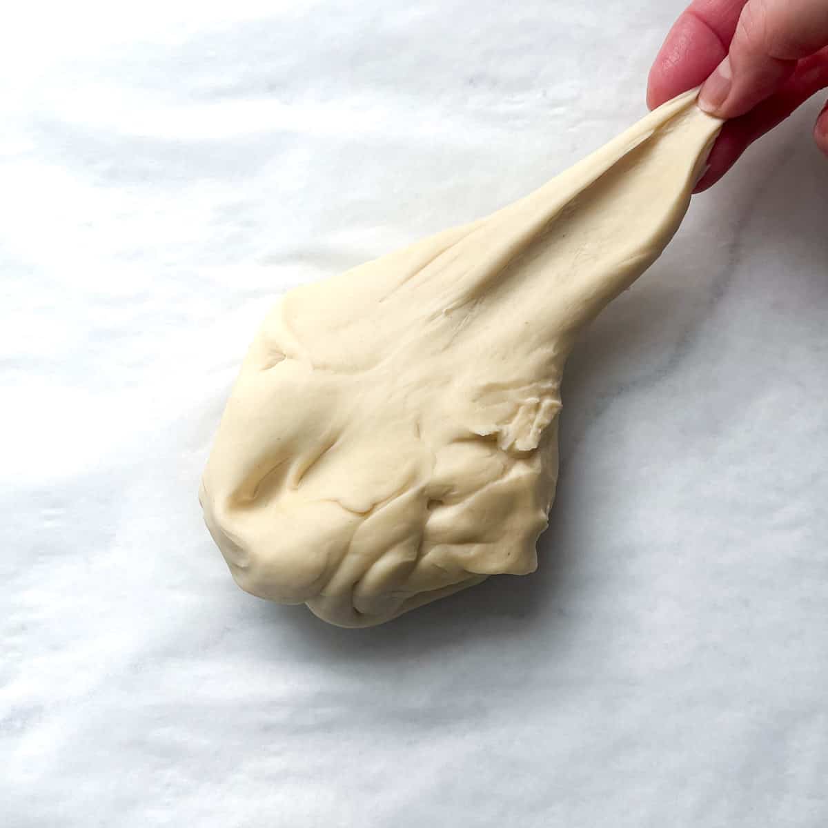 Flammkuchen dough being stretched to demonstrate elasticity.
