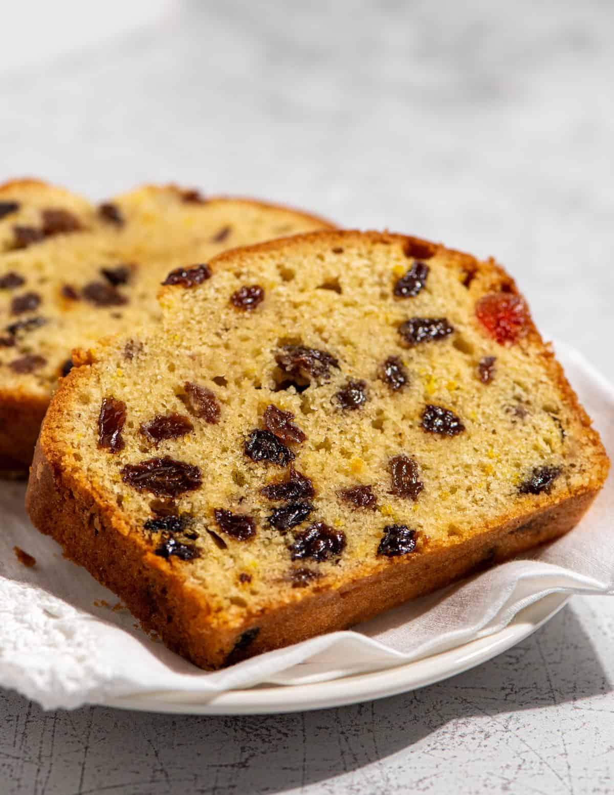 Close-up of two slices of sultana cake with glacé cherries on a white plate.
