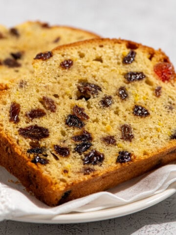 Close-up of two slices of sultana cake with glacé cherries on a white plate.
