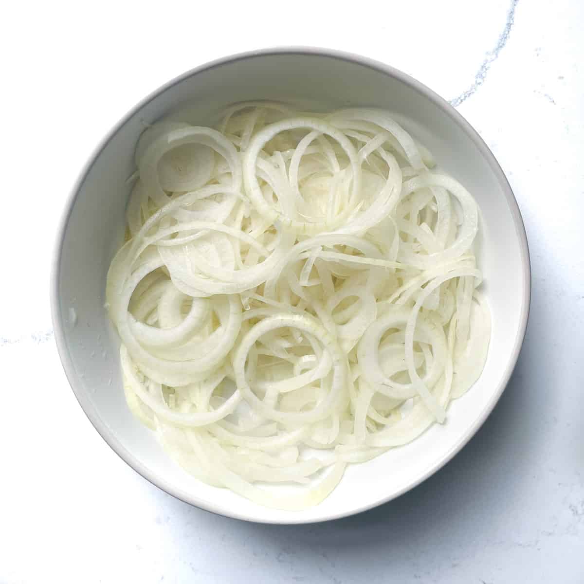 Finely sliced onions in a white bowl.