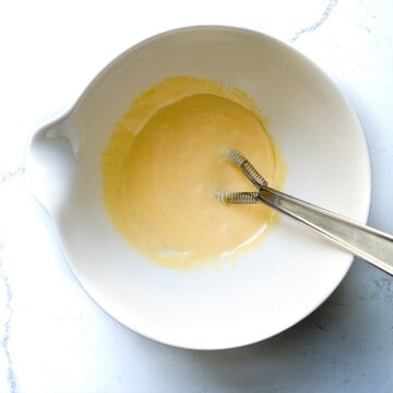 Whisking egg yolks and sugar in a white mixing bowl.
