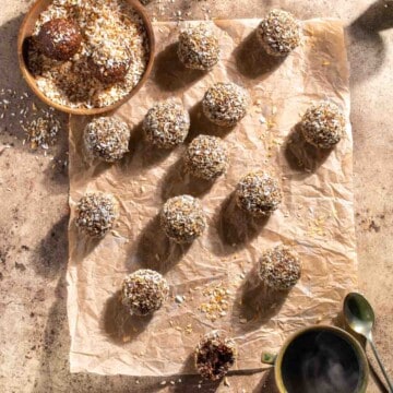 Chokladbollar on a piece of brown paper surrounded by a bowl of desiccated coconut and two mugs of coffee.