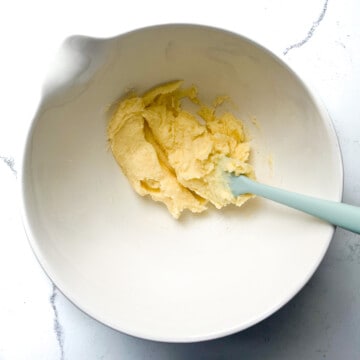 Butter and sugar being mixed together in a large white mixing bowl.