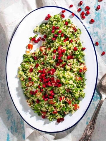 Taboule salad on a white oval plate, scattered with pomegranate seeds.