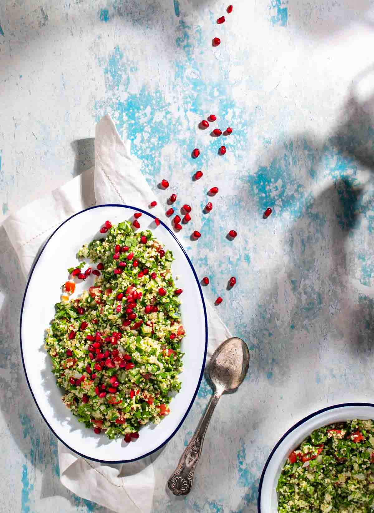 Taboule salad on a white oval plate, scattered with pomegranate seeds. 