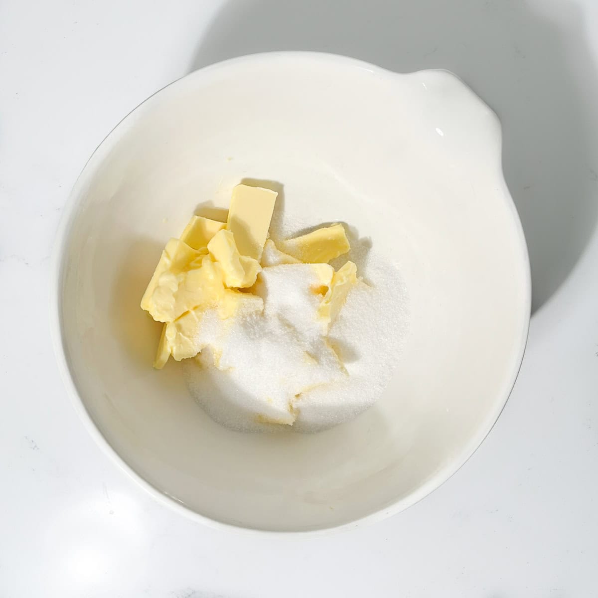 Adding butter and sugar to a large white bowl.