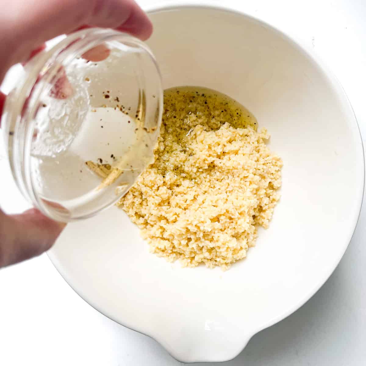 Adding the salad dressing to the bulgur wheat in a large white bowl.