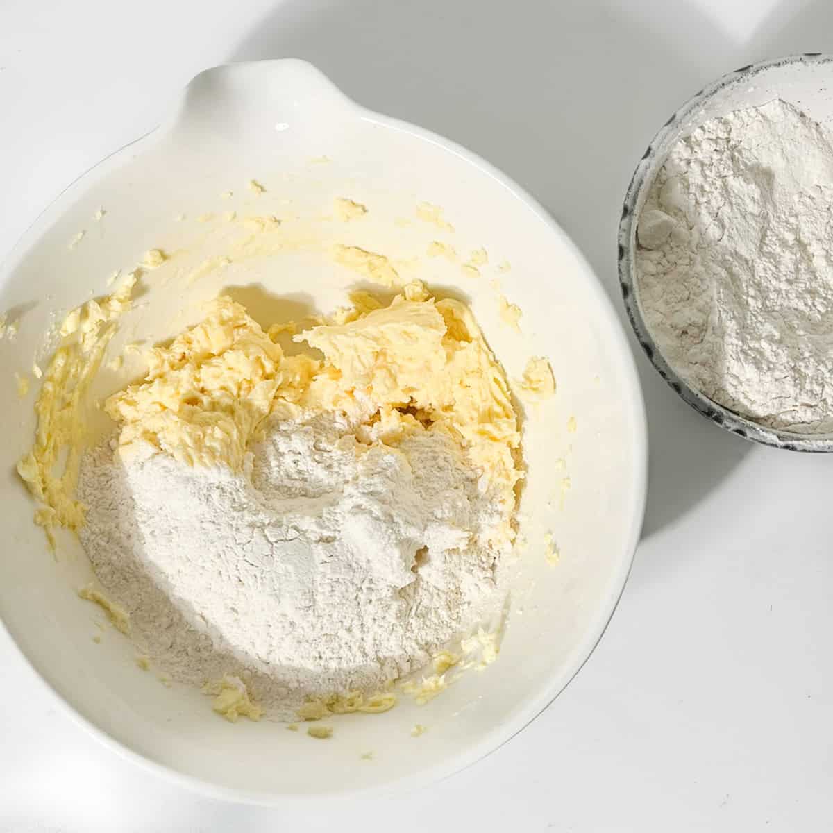 Adding flour to the bowl of thumbprint icing cookie dough.