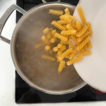 Adding dried pasta to a pan with rapidly boiling water.