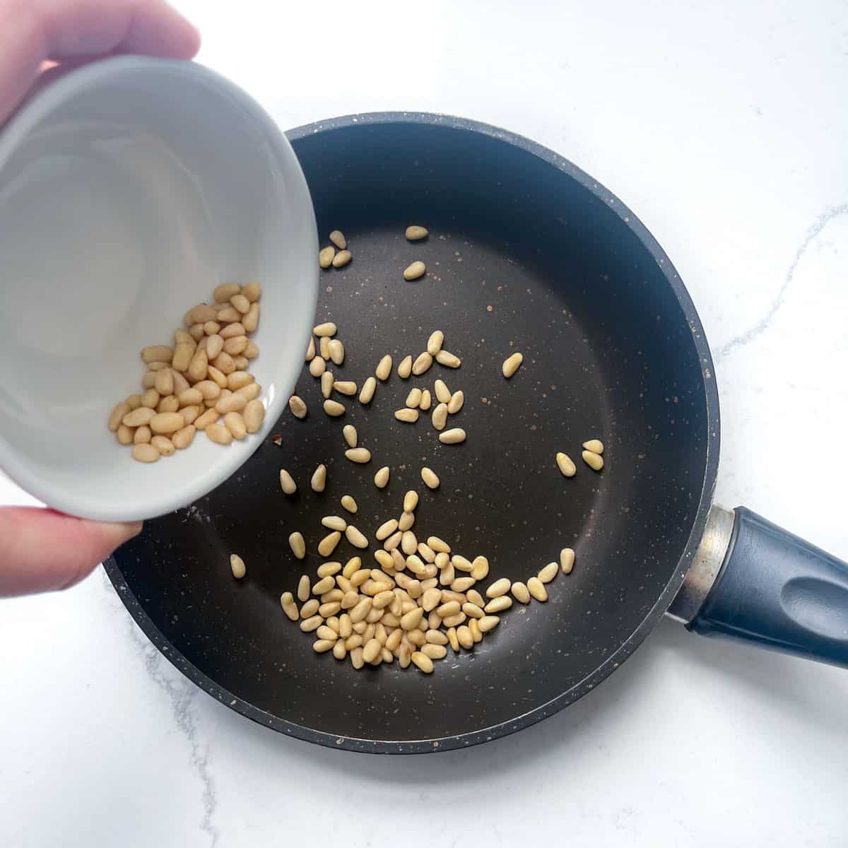 Adding pine nuts to a frying pan for roasting.