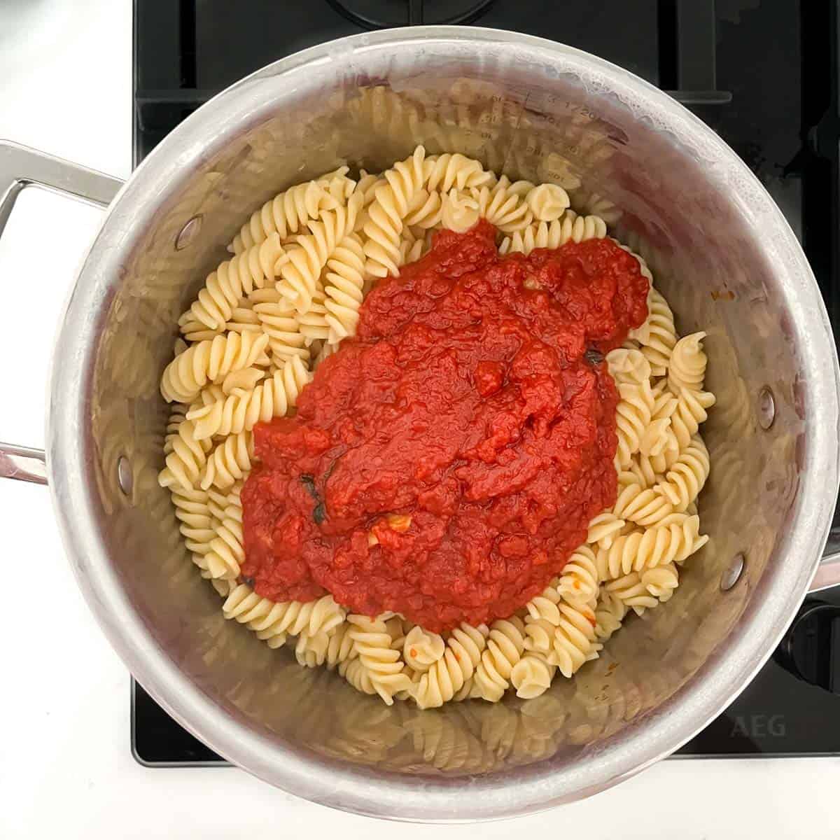Tomato sauce added to a pan of cooked pasta.