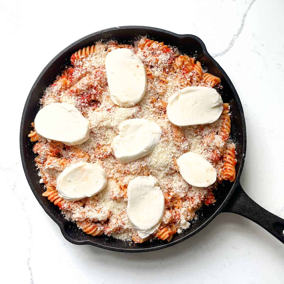 A completed pasta alla sorrentina in a black cast iron pan, ready to go into the oven.