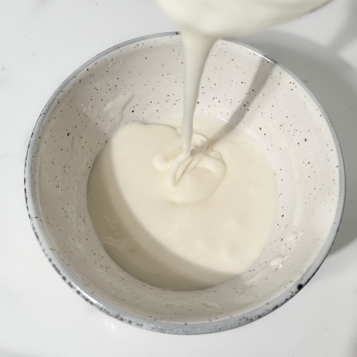 Demonstrating the consistency of the runny frosting for thumbprint cookies in a small white bowl.