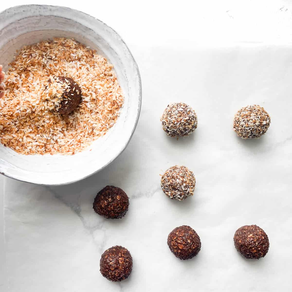 Chokladbollar being covered with toasted coconut.