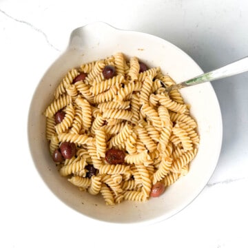 Salad dressing for pasta fredda mixed in with pasta in a large white bowl.