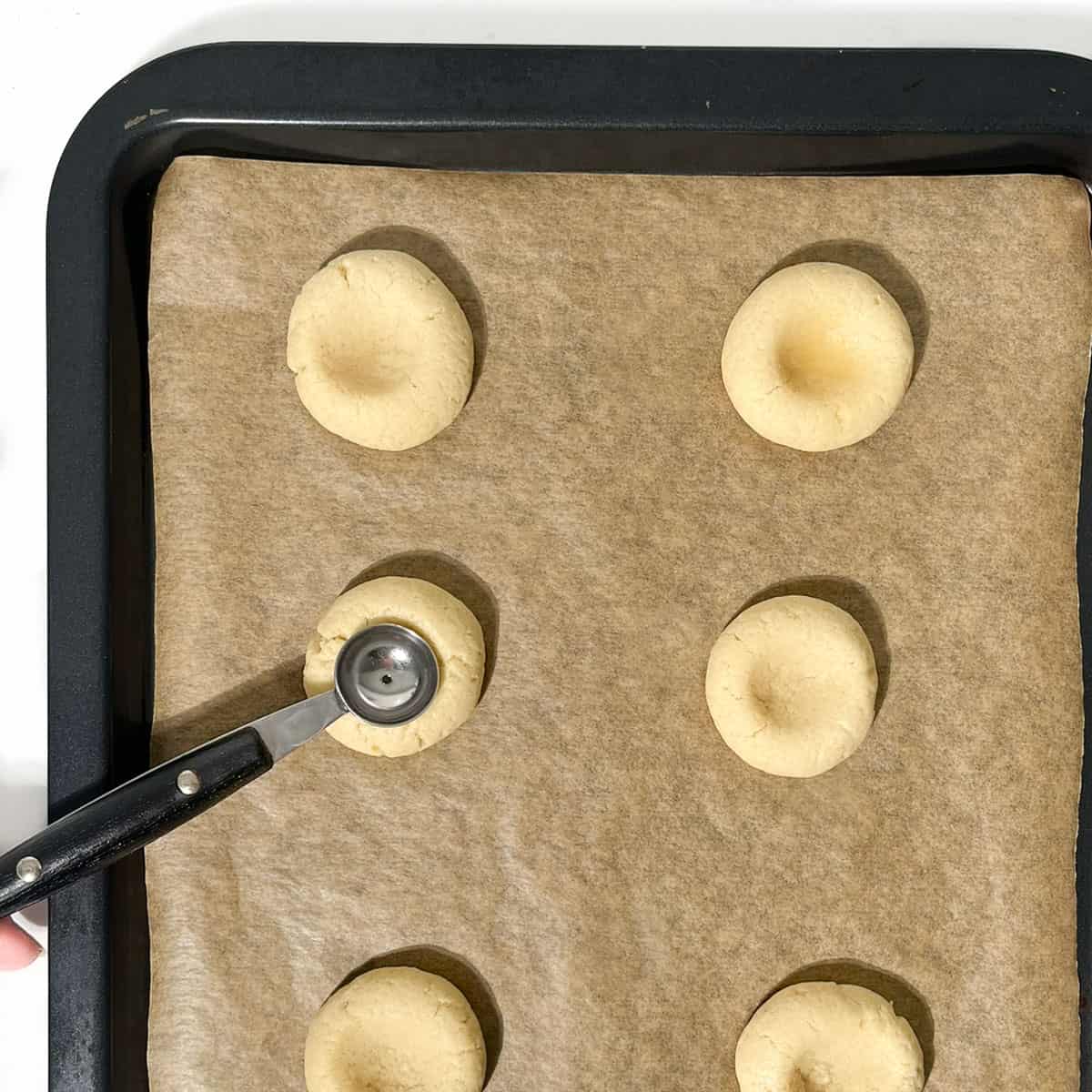 Indenting half-baked thumbprint cookies with a small melon baller on a baking tray.