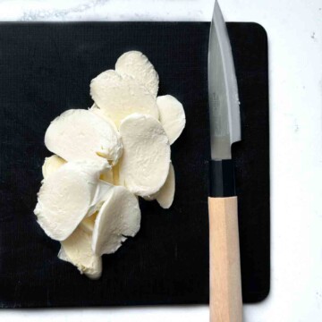 Mozzarella slices on a black chopping board.