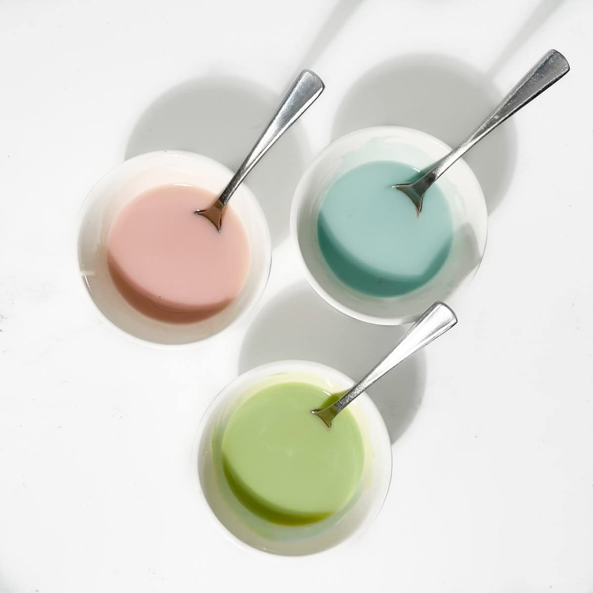 Three small bowls of blue, green and pink icing.