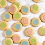 Pink, blue and green thumbprint icing cookies scattered across a white service.