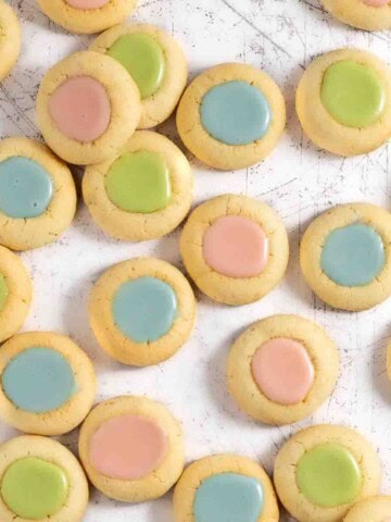 Pink, blue and green thumbprint icing cookies scattered across a white service.