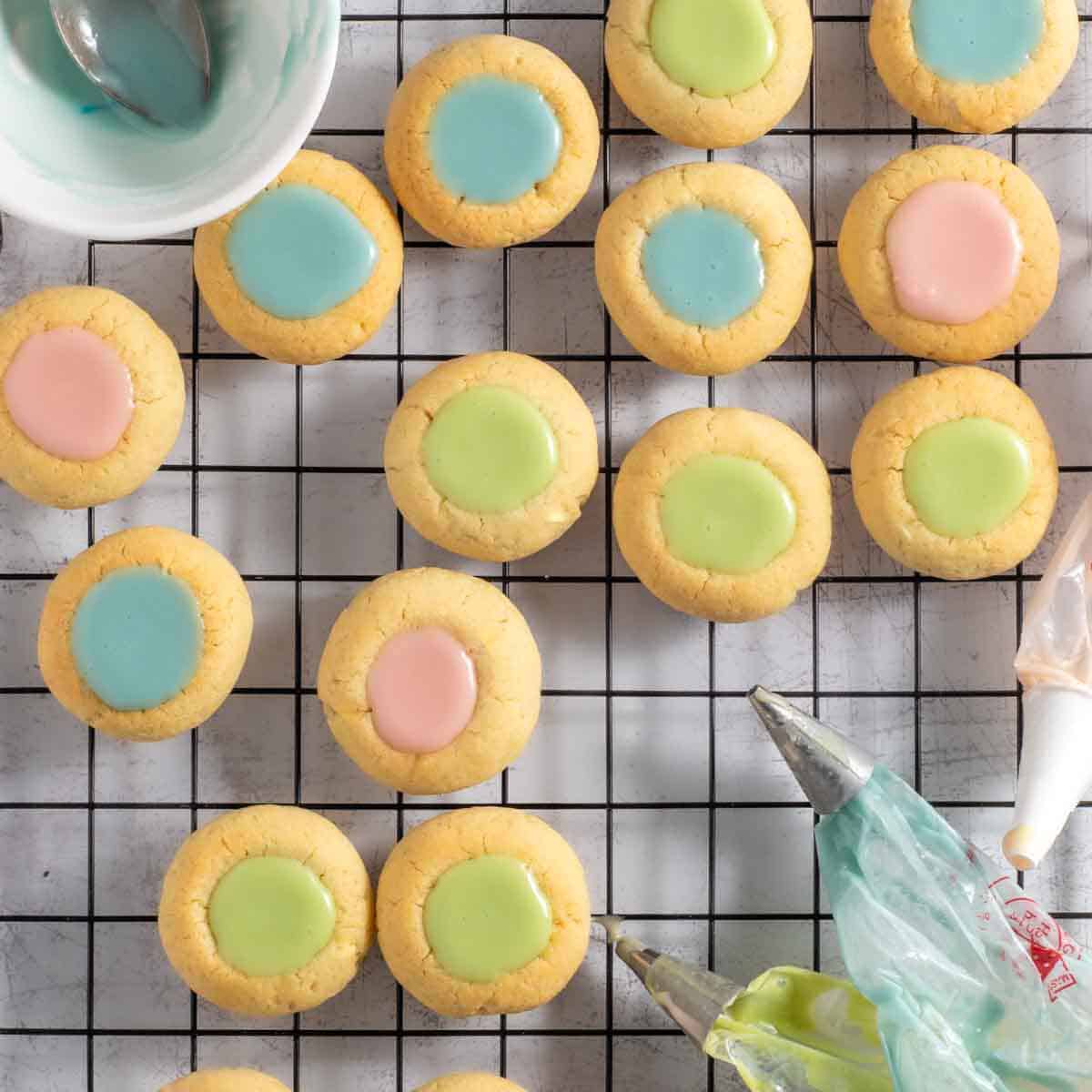 Thumbprint icing cookies on a wire cooling rack surrounded by piping bags.