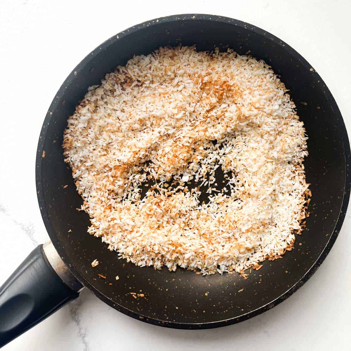 Toasted desiccated coconut in a small frying pan.