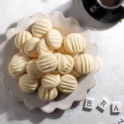 Sequilhos cookies on a white plate with two cups of coffee and some scrabble pieces.