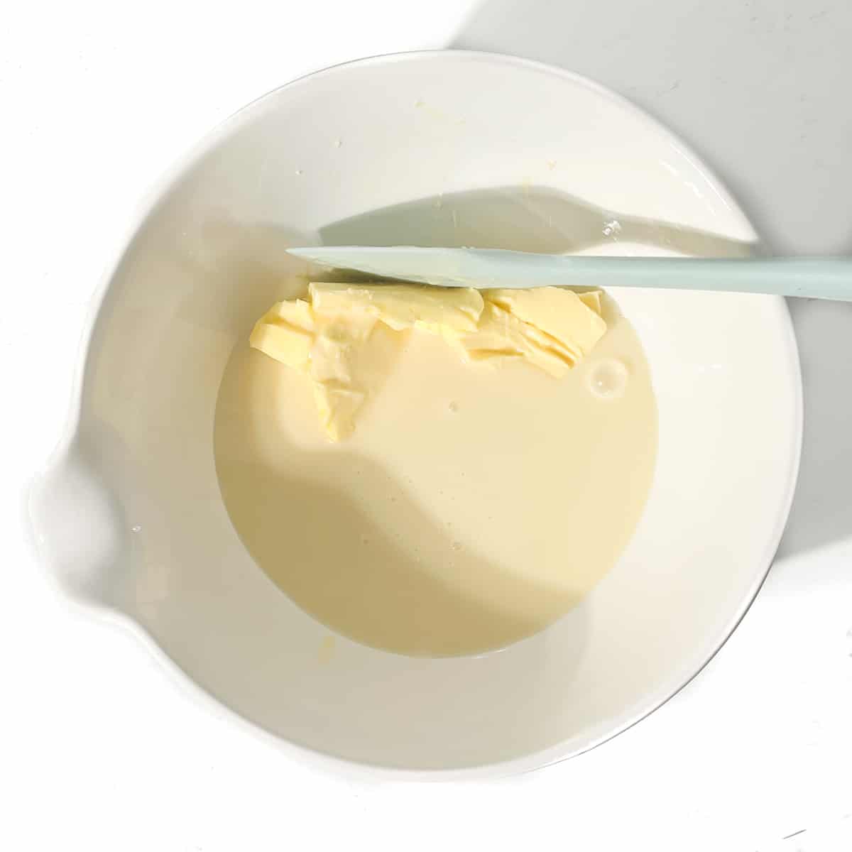 Adding condensed milk and butter to a large white bowl.