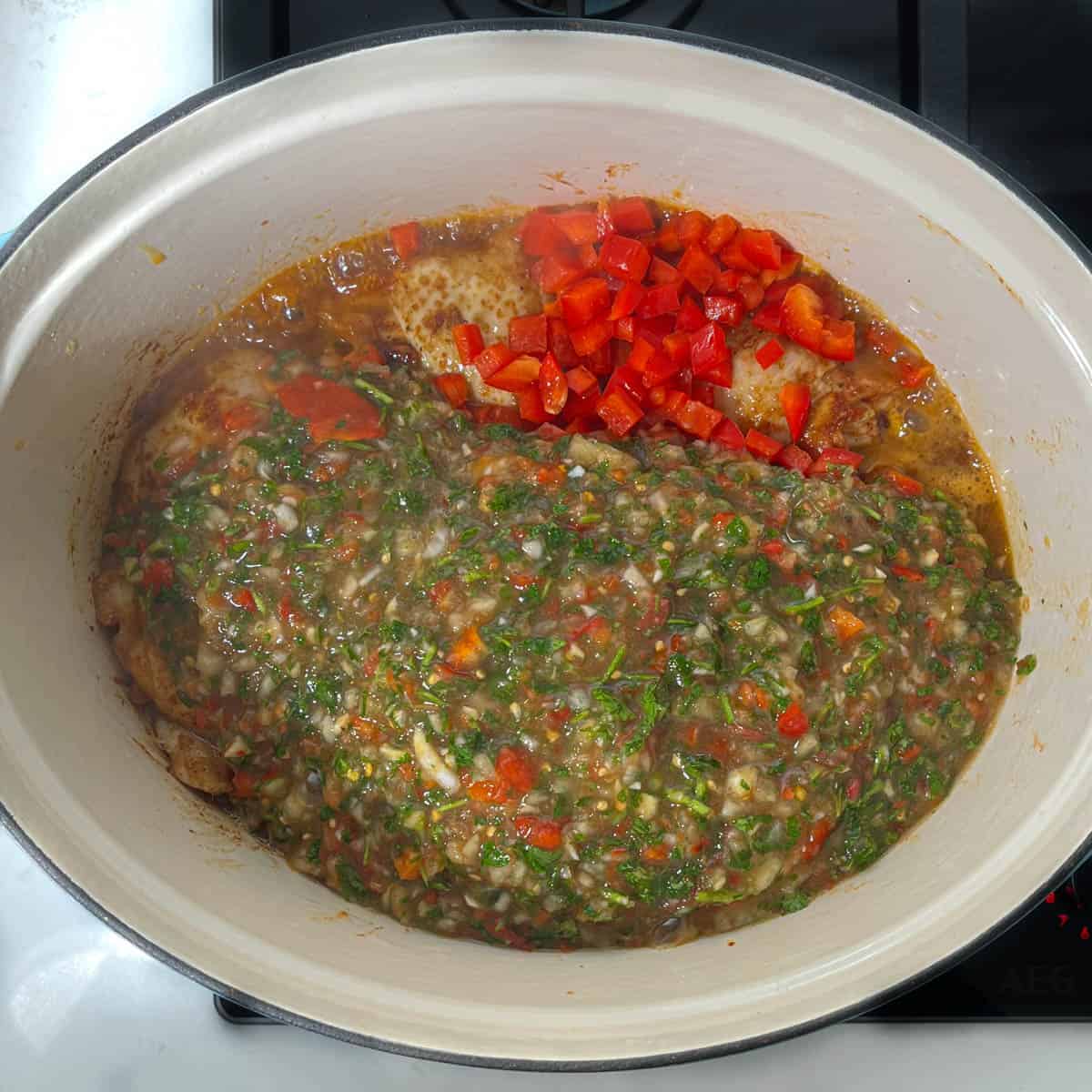 Adding the deco de pollo sauce and chopped pepper to the chicken in a dutch oven.