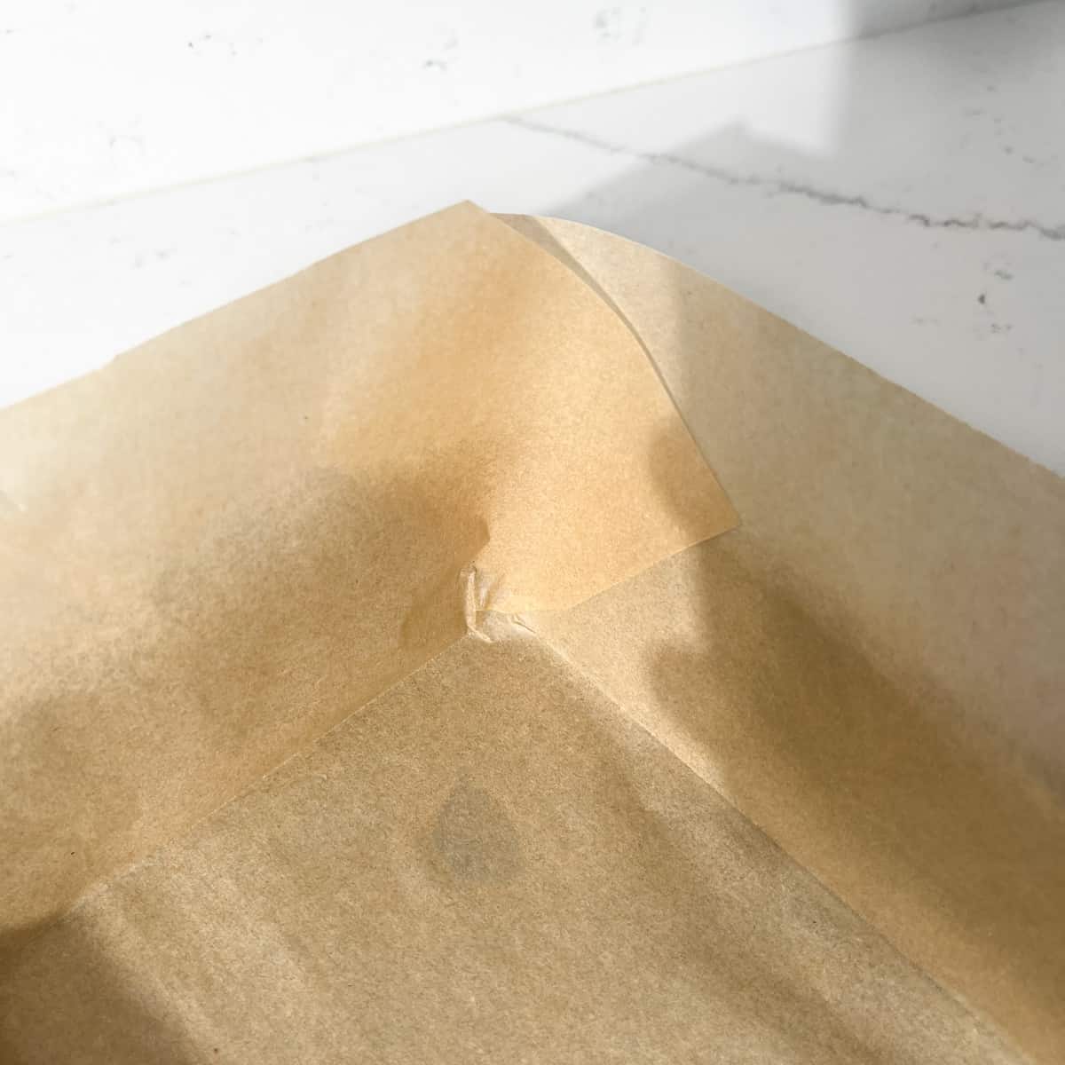 Overlapping corners of baking paper lining a baking tin.