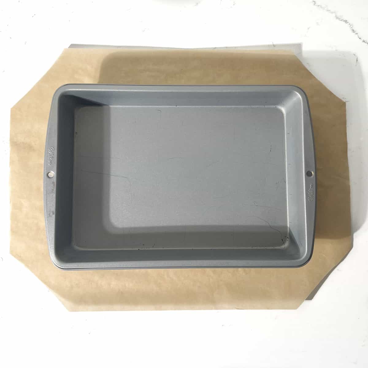 A baking tin on a rectangular piece of baking paper with all four corners cut off.