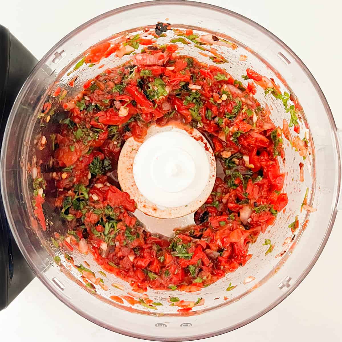 Red chimichurri ingredients in a food processor, chopped before adding olive oil.