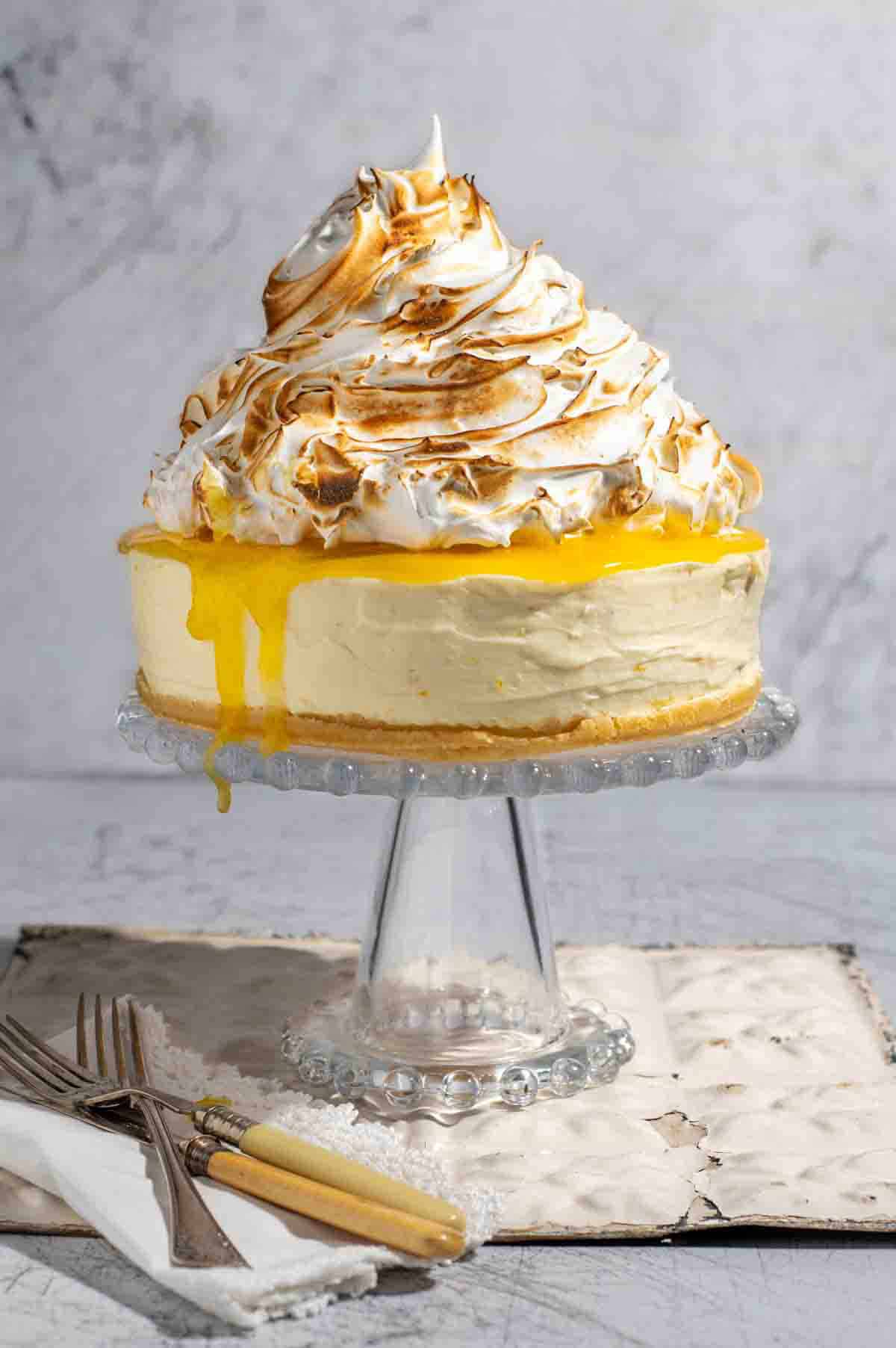 Lemon meringue cheesecake on a glass cake stand.