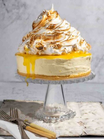 Lemon meringue cheesecake on a glass cake stand.