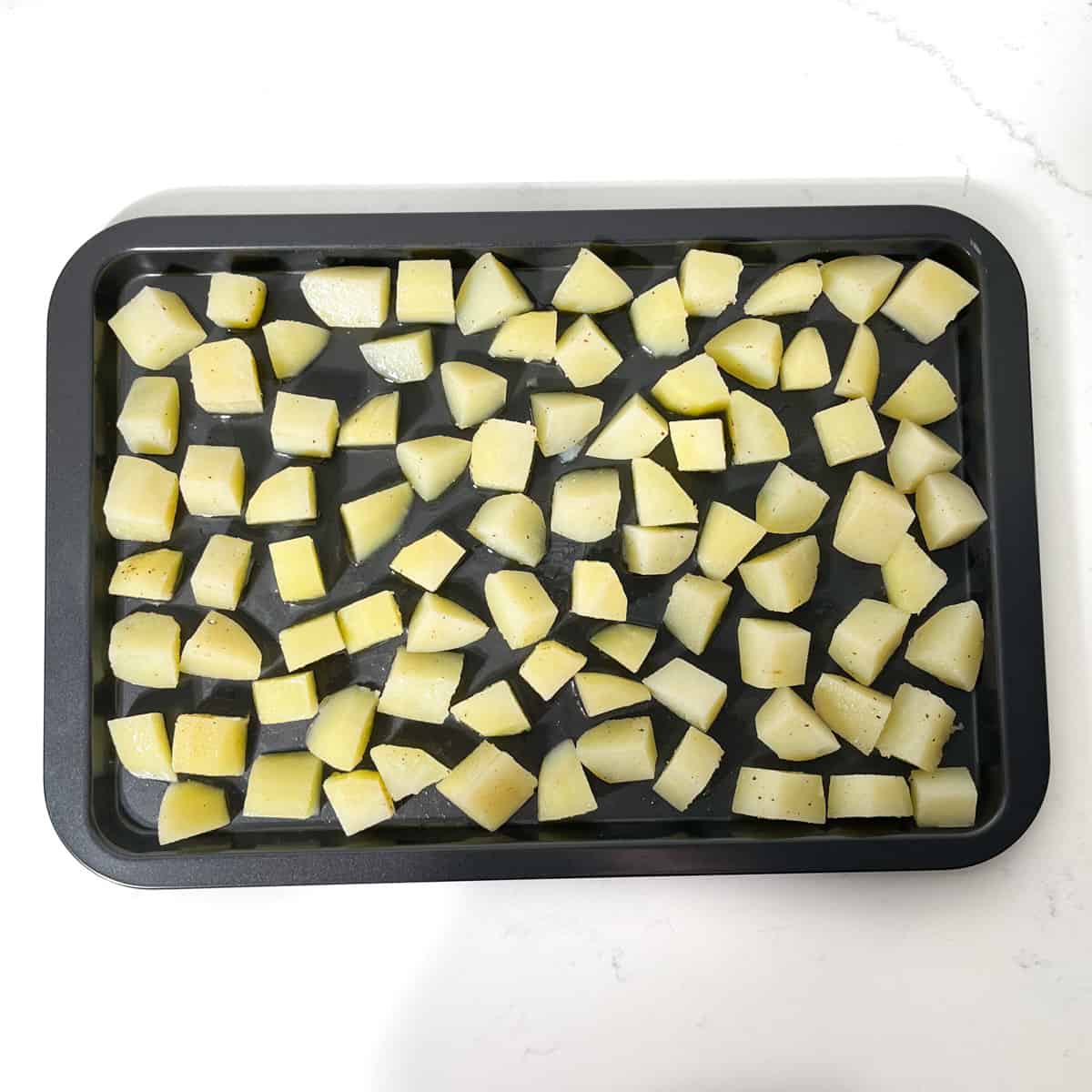 Parmentier potato cubes spread out on a baking tray in a single layer.