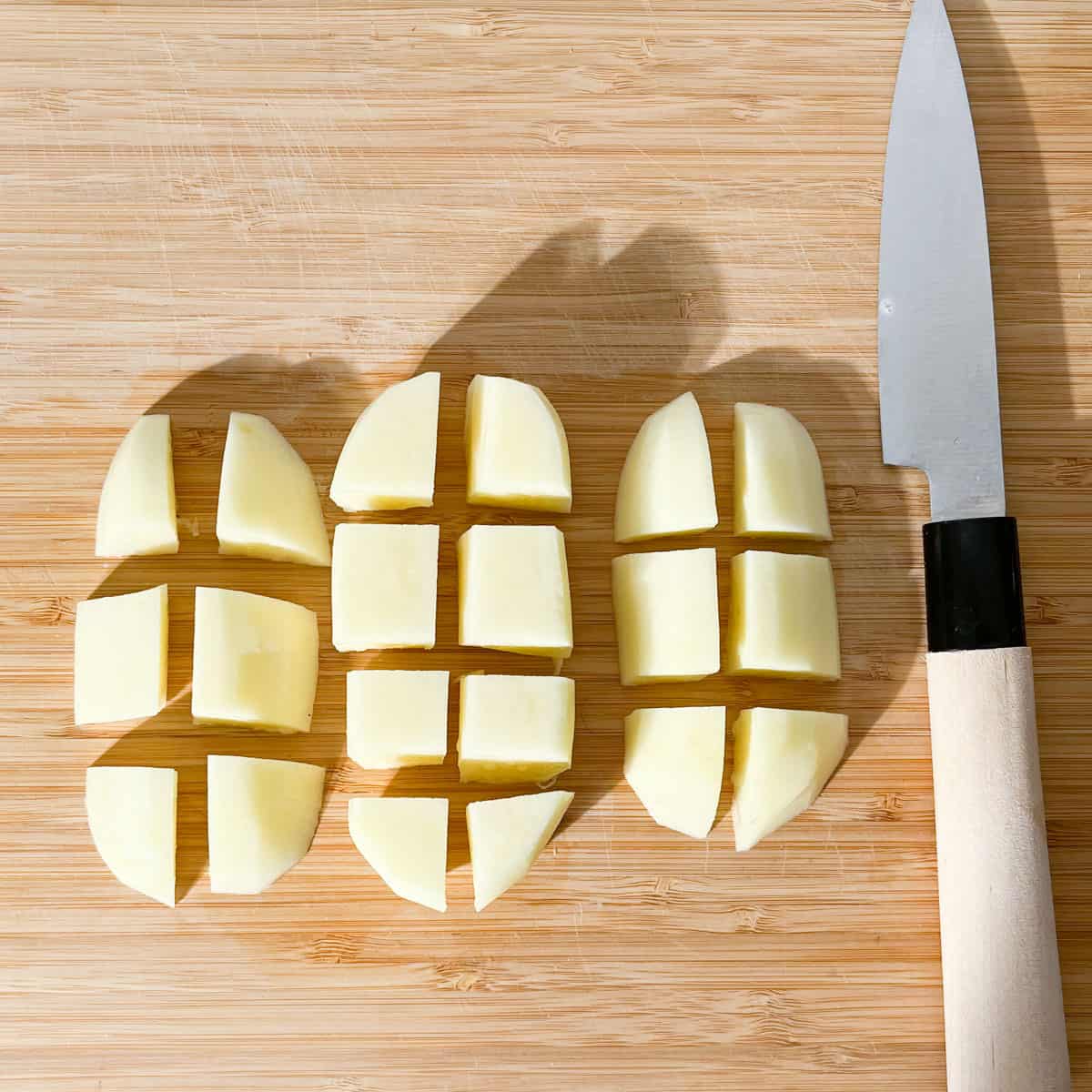 A potato on a cutting board cut into cubes.