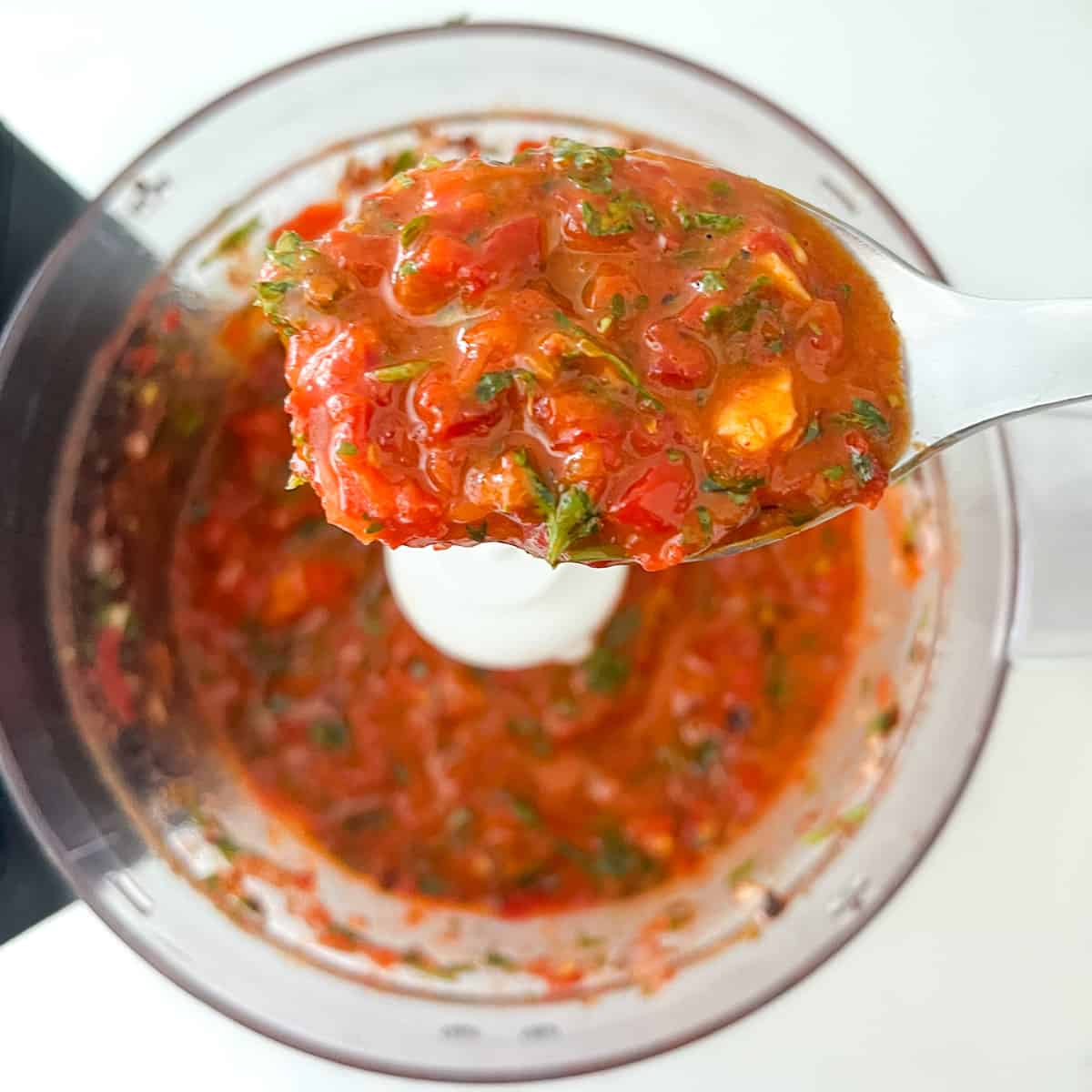 Red chimichurri ingredients in a food processor, chopped after adding olive oil.