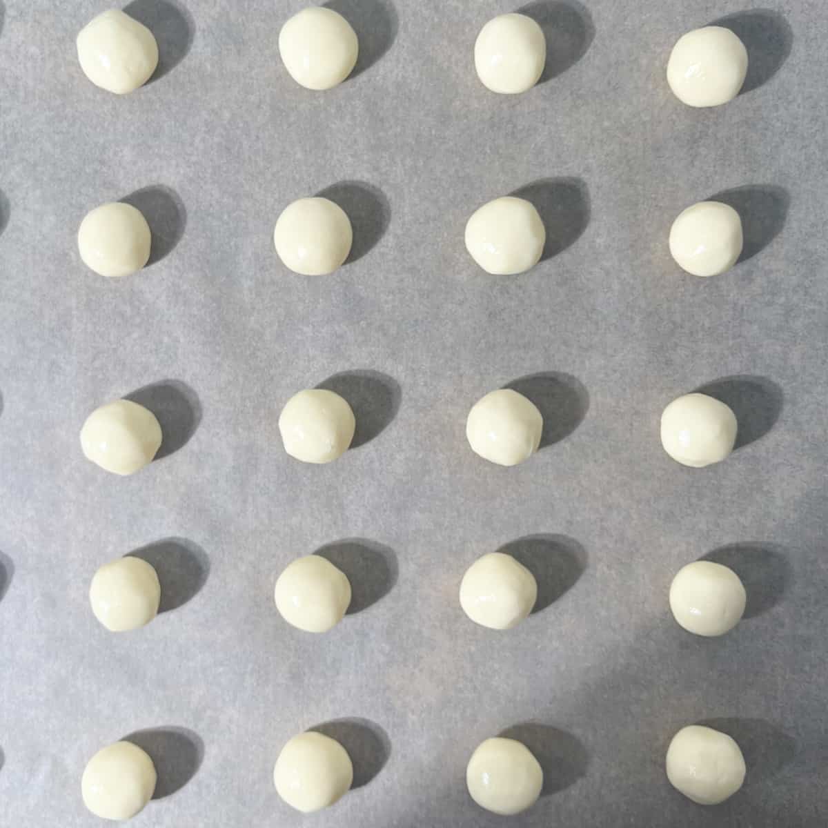 Dough balls on a large baking tray, ready to be flattened with a fork.