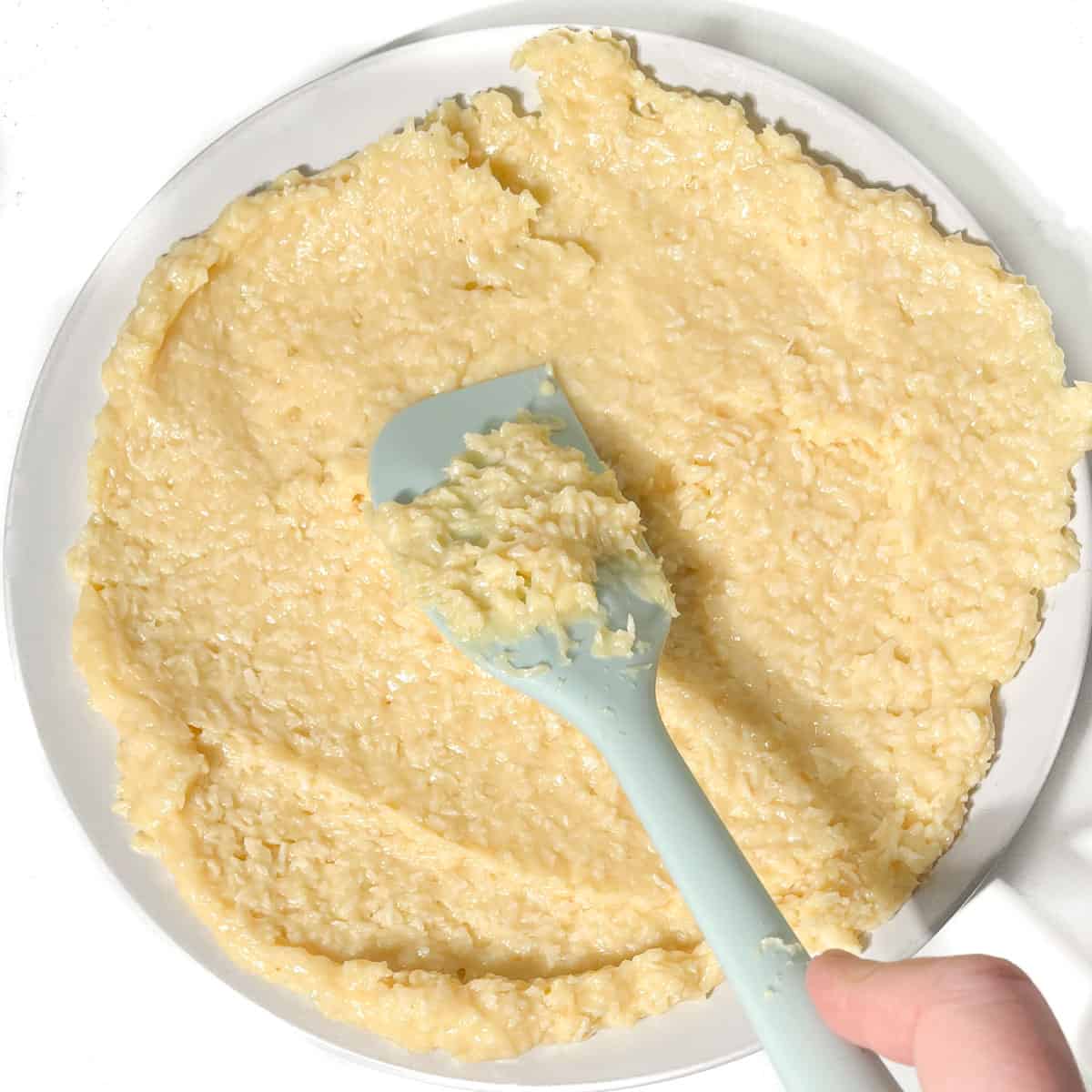 The Beijinhos mixture being spread out thinly on a plate with a rubber spatula.