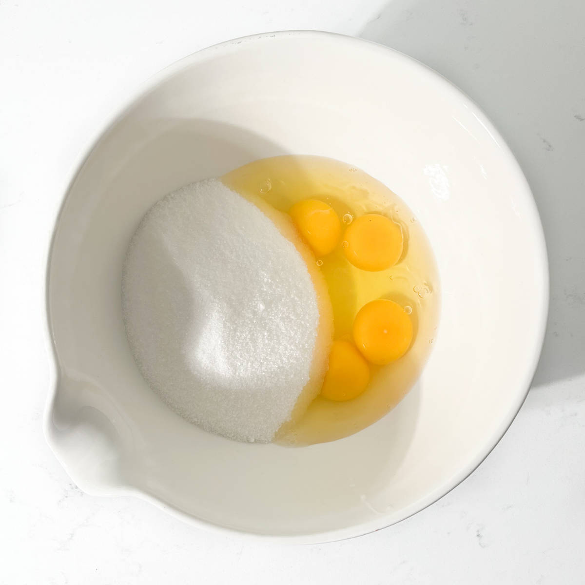 Sugar and eggs added to a large white bowl.