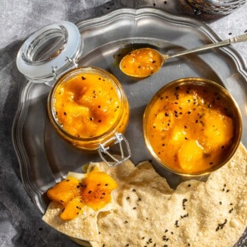 Indian mango chutney in a jar and a bowl with some poppadoms on a plate.