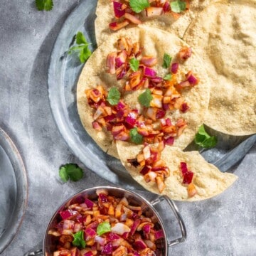 Indian onion chutney spread over poppadoms on a grey background.