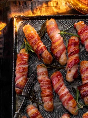 Cooked Pigs in blankets on a baking tray next to a bottle of whiskey.
