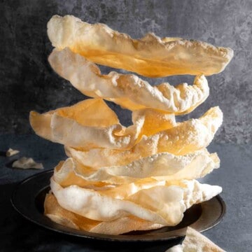 A pile of poppadoms on a plate against a grey background.