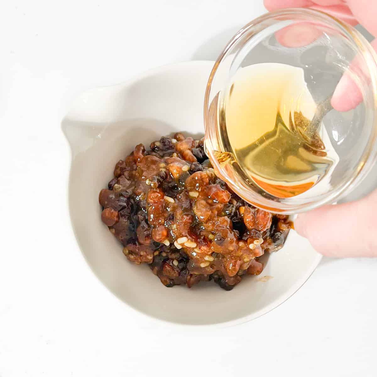 Pouring brandy into a small bowl with minced meat. 