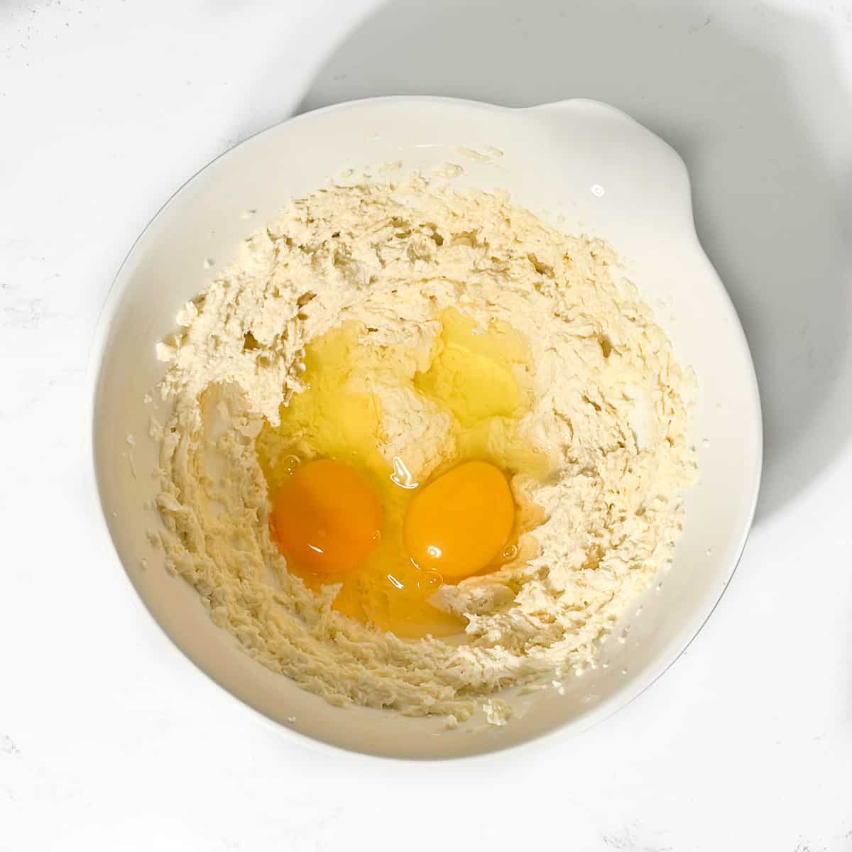 Adding eggs to the frangipane mixture in a white bowl.