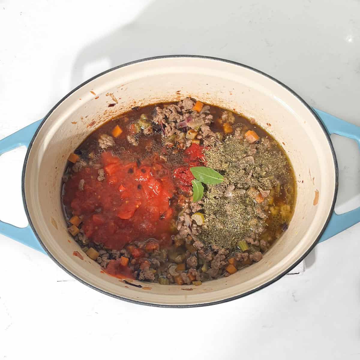 Adding tomatoes and herbs to the pot for the mince and dumplings.