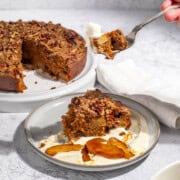 A slice of spiced apple cake on a light grey plate with some cream and caramelised apples.