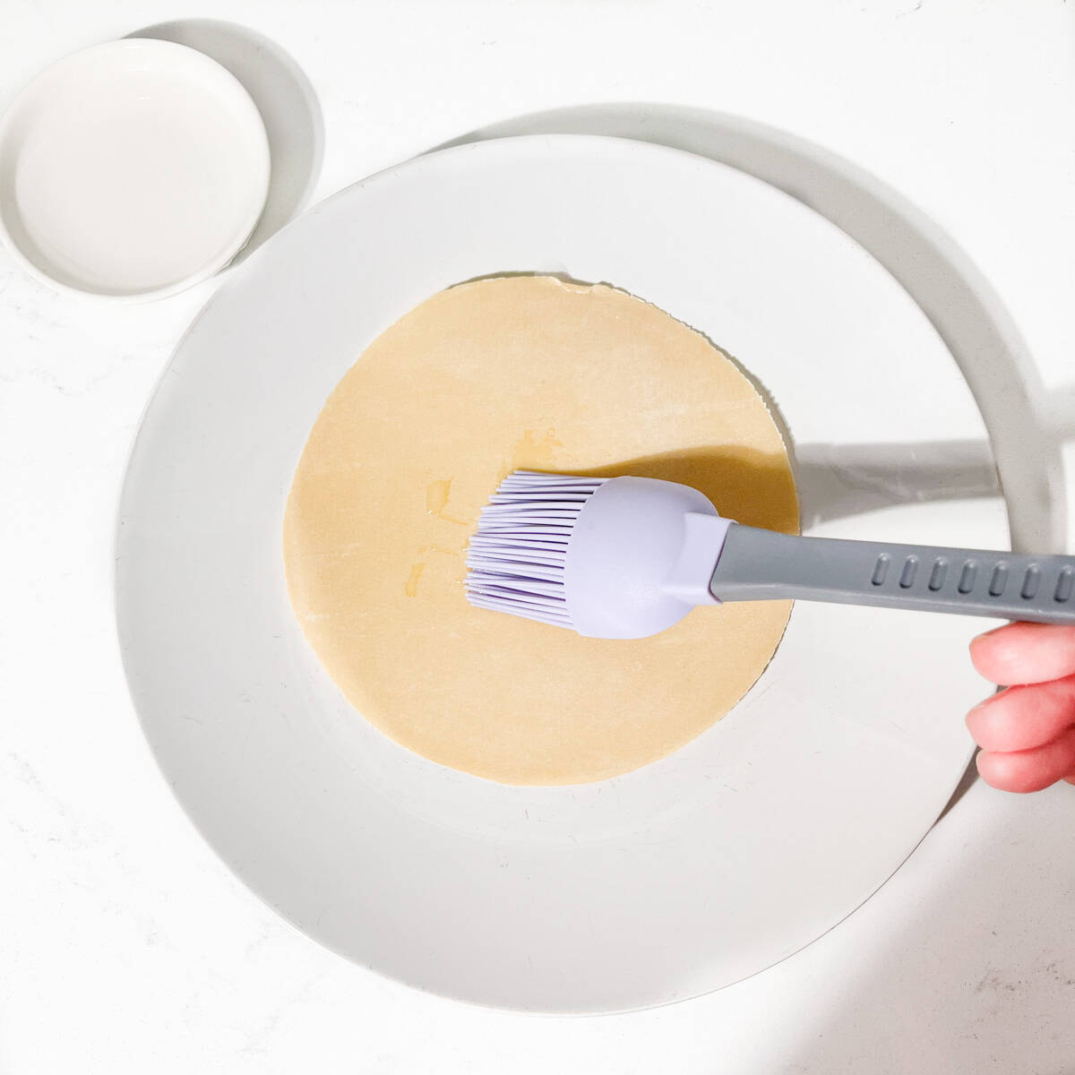 Brushing an uncooked poppadom with water using a pastry brush.