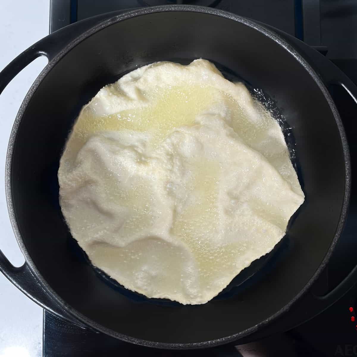 A fried poppadom in oil in a black saucepan.